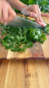 Chopping fresh green parsley on a wooden cutting board with a knife.
