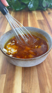 Whisking oil with garlic slices in a ceramic bowl.