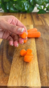 Hand holding sliced carrots on wooden cutting board.