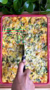 Hand cutting baked egg casserole with spinach and vegetables.