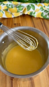 Stainless steel bowl with whisk, mixing smooth yellow lemon curd.