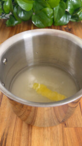 Stainless steel pot with lemon peel and liquid on wooden surface