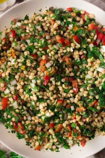 Close-up of a colorful pearl couscous tabouleh salad with parsley, tomatoes, and herbs in a white bowl.