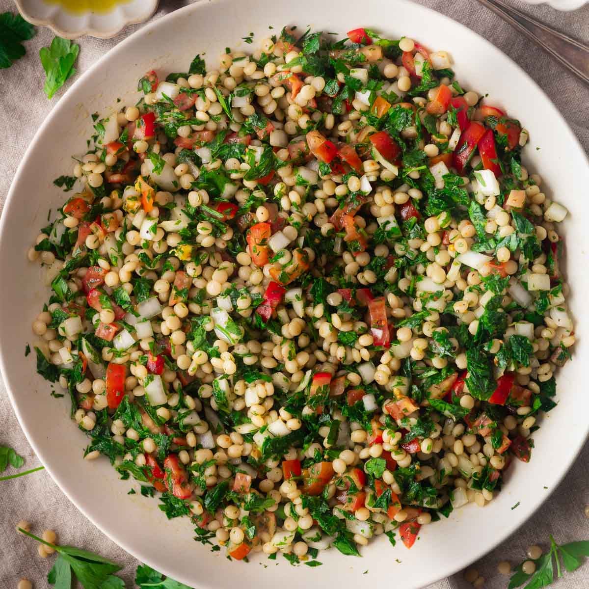 Close-up of a colorful pearl couscous tabouleh salad with parsley, tomatoes, and herbs in a white bowl.