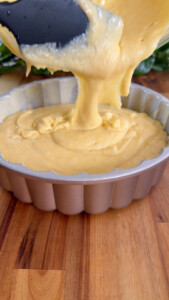Pouring cake batter into a fluted pan on a wooden surface.