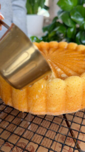 Pouring liquid over a cake on a cooling rack.