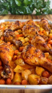 Roasted chicken drumsticks with carrots and potatoes on a baking sheet.