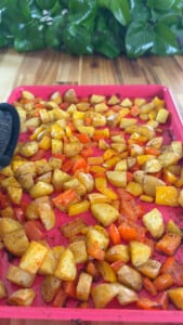 Roasted diced potatoes and bell peppers on a pink baking tray.