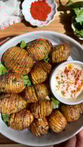 Hasselback potatoes with herbs and a dip, garnished with paprika.