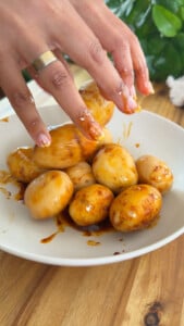 Hand tossing marinated potatoes in sauce.