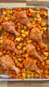 Raw chicken drumsticks, diced carrots, and potatoes on a baking sheet.