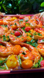 Close-up of seasoned shrimp with cherry tomatoes, asparagus, and fresh herbs.