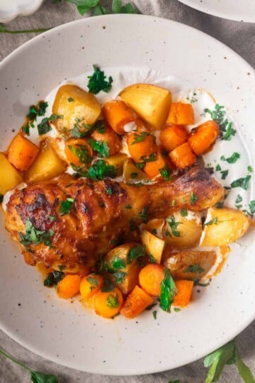 Baked red pepper and garlic drumsticks with potatoes, carrots, and fresh parsley garnish on a white plate.