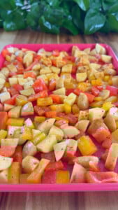 Diced red and yellow bell peppers and potatoes on a pink tray.