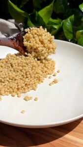 Wooden spoon scooping pearled couscous onto a white plate.
