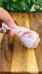Hand holding a raw chicken drumstick with a cut.