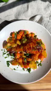 Grilled chicken drumstick with glazed carrots and potatoes, garnished with fresh herbs on whipped feta.