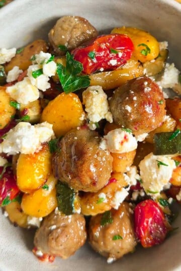 Sheet pan baked gnocchi with vegetables, feta cheese, and meatballs garnished with parsley.
