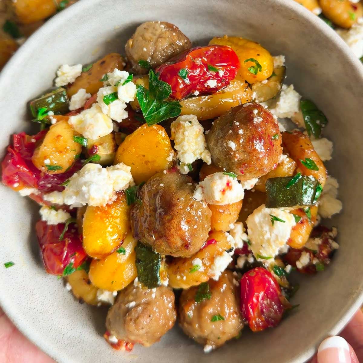 Sheet pan baked gnocchi with vegetables, feta cheese, and meatballs garnished with parsley.