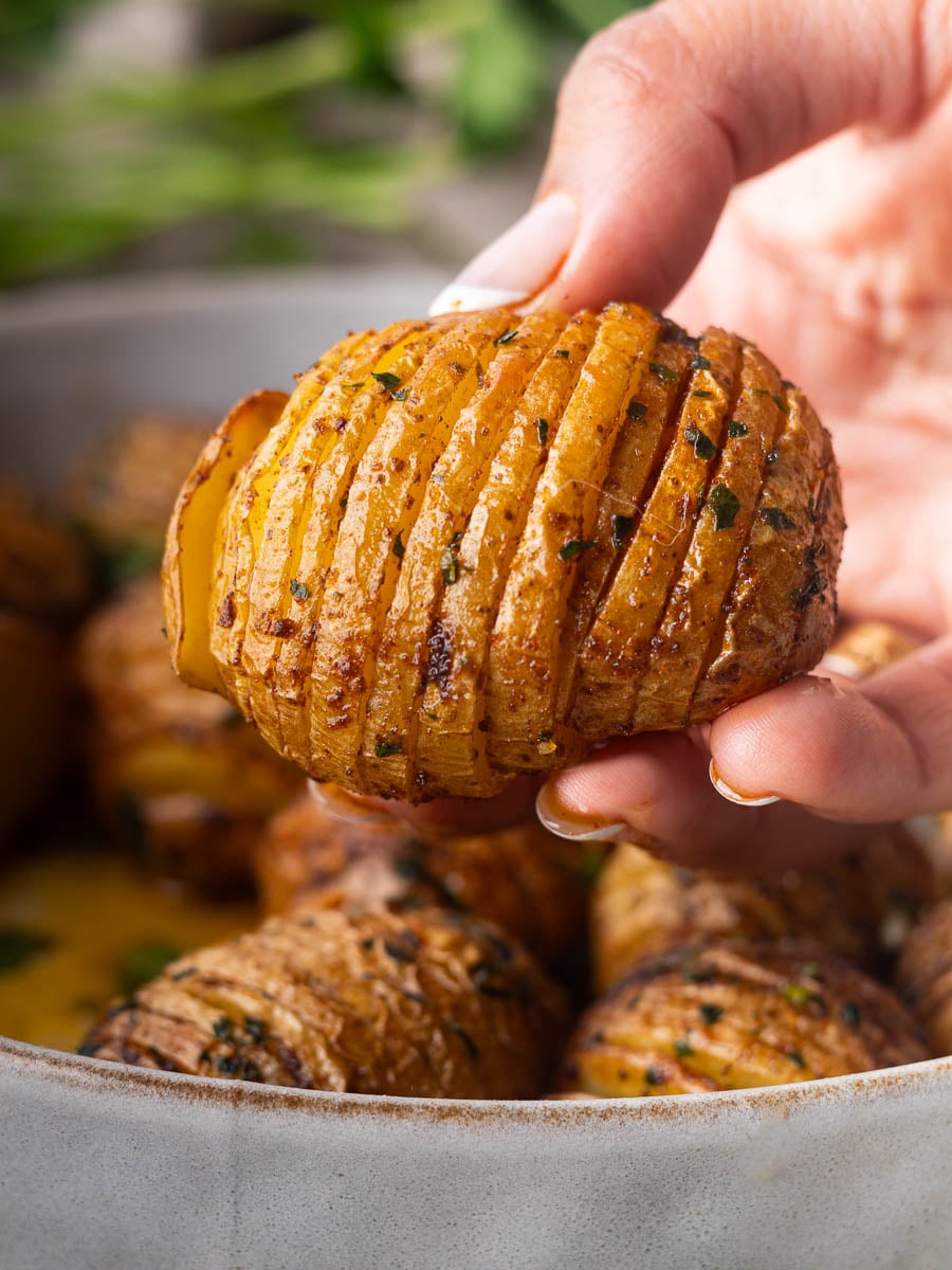 Hand holding a sliced smoky air fryer Hasselback potato in a bowl with other potatoes.