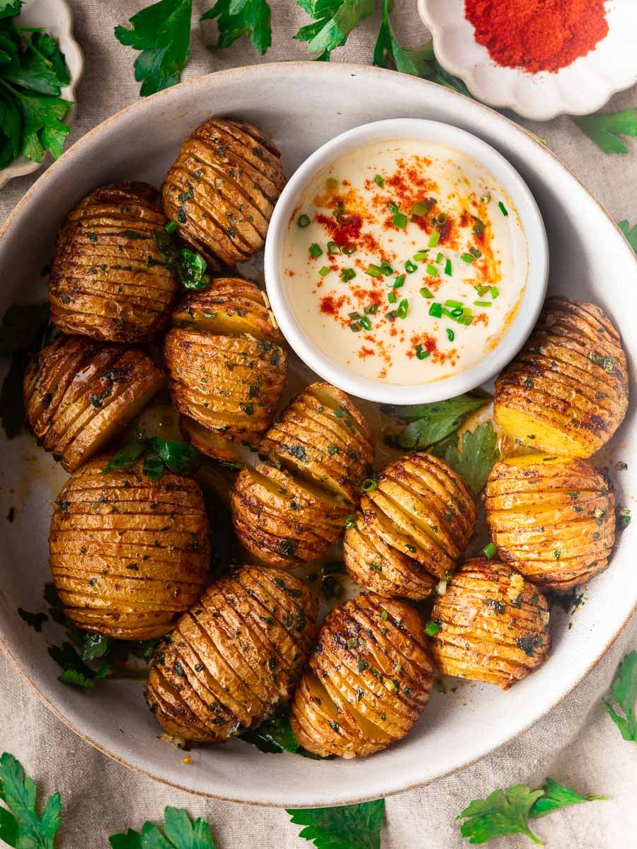 Smoky air fryer hasselback potatoes with herbs on a plate, served with a creamy dipping sauce, garnished with chives and paprika.