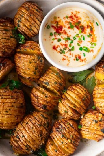 Smoky air fryer hasselback potatoes with herbs and a creamy dipping sauce garnished with paprika and chives in a bowl.