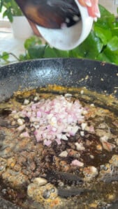 Chopped onions being added to a sizzling pan with melted butter and spices.