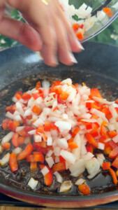 Chopped onions and red peppers being added to a sizzling pan.