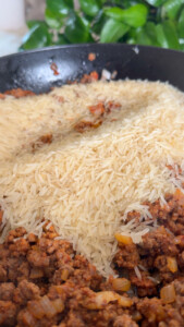 Ground beef and uncooked rice in a pan with green leaves in the background.