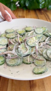 Cucumber salad with red onion and creamy dill dressing in a white bowl.