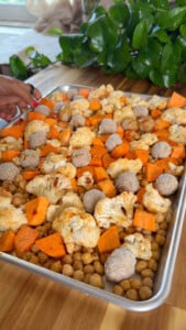 Sweet potatoes, cauliflower, meatballs, and chickpeas on a baking sheet.