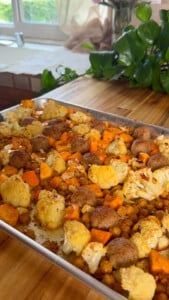 Roasted vegetables with meatballs on a baking sheet, featuring cauliflower, sweet potatoes, and chickpeas.