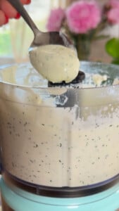 Food processor with creamy herb sauce on spoon.