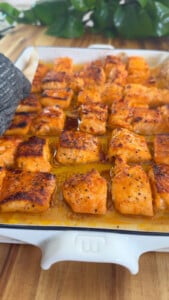 Baked salmon bites arranged in a baking dish on a wooden table.