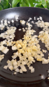 Chopped onions and garlic sizzling in a black frying pan.