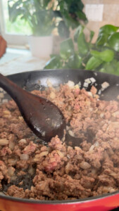 Cooking ground beef and onions in a pan with a wooden spoon.