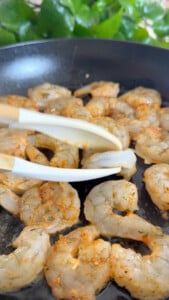 Cooking seasoned shrimp in a pan with tongs.