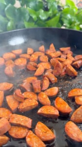 Sliced chorizo sausages sizzling in a frying pan.