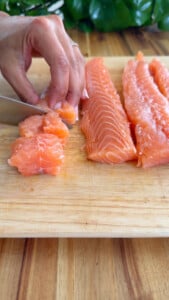 Hand slicing raw salmon fillet on a wooden cutting board.