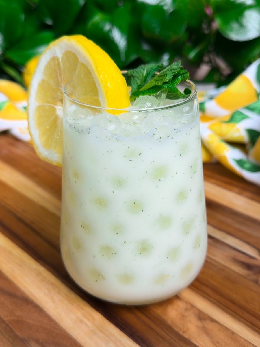 Egyptian lemonade in a glass with lemon slice garnish, wooden table, vibrant green background.
