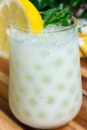 Egyptian lemonade in a glass with ice cubes, garnished with a lemon slice and mint leaves on a wooden table.