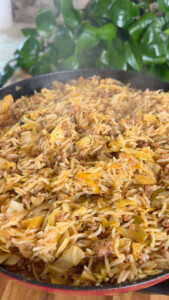 Close-up of a pan with steaming rice mixed with ground meat and vegetables.