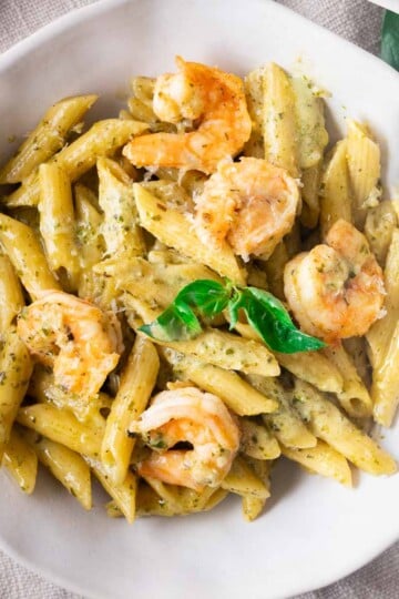 Pesto shrimp pasta garnished with fresh basil, served in a white bowl.