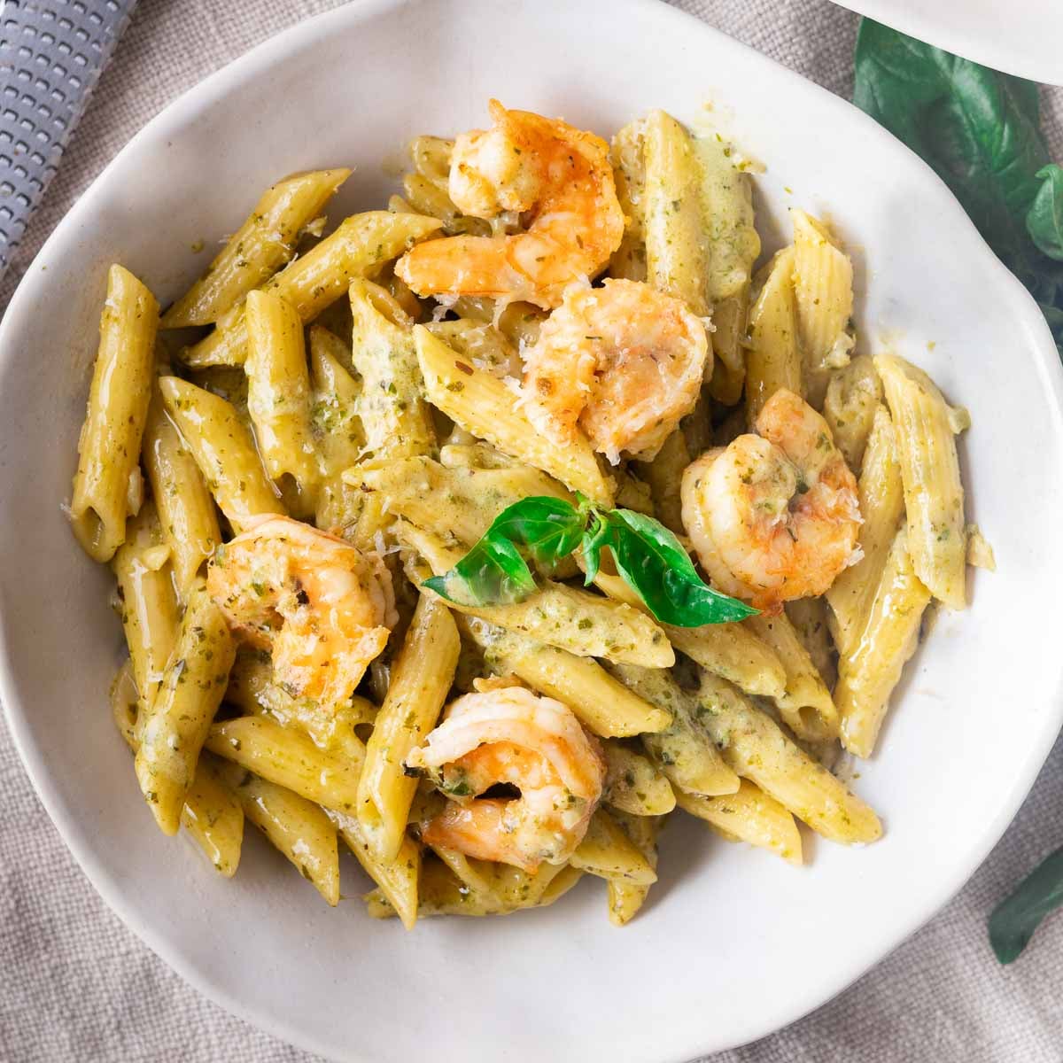 Pesto shrimp pasta garnished with fresh basil, served in a white bowl.