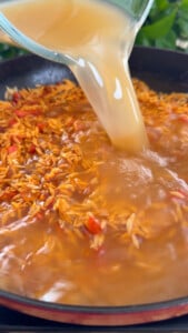 Pouring broth into a skillet with orzo.