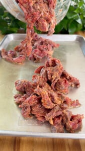 Raw marinated beef strips being placed on a metal baking tray.