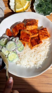 Grilled salmon with rice and cucumber salad in a white bowl, lemon and dill on the side.