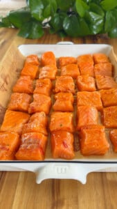 Diced raw salmon pieces in a white baking dish.
