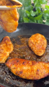 Grilled chicken breasts sizzling in a pan.