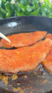 Seasoned chicken fillets cooking in a skillet.